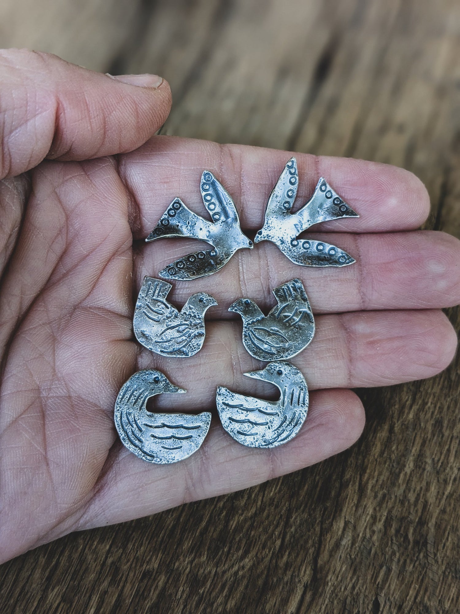 Hand holding sterling silver post earrings that are a flying bird, folk art chicken, and loon.
